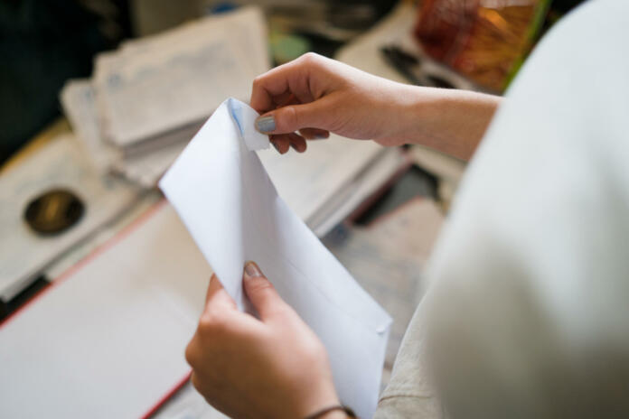 Close up on girl female woman hands holding and opening white envelope by the table at office work or at home with bills mail or insurance contract invoice letter