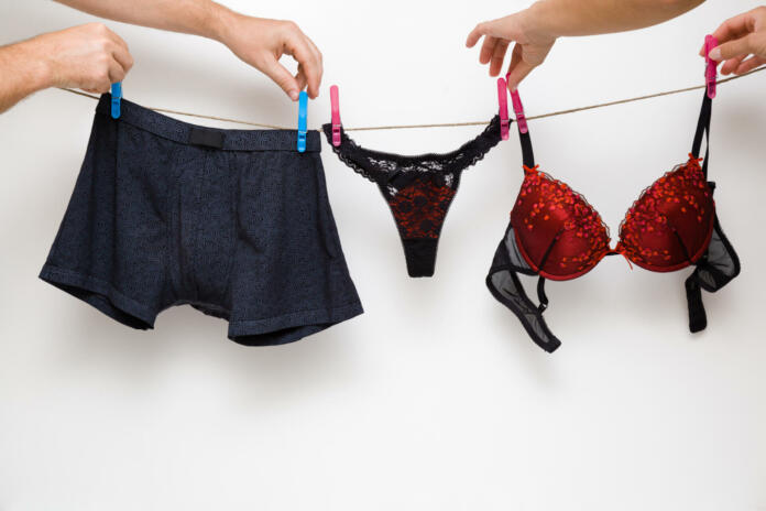 Man's and woman's hands together hanging clean black and red undergarment. Underwear drying on laundry rope at white wall. Dry cleaning. Regular washing. Couple's daily routine. Relationships concept.