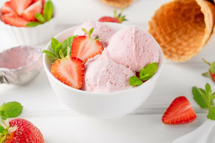 Strawberry ice cream with fresh berries in a bowl on a white wooden background. Selective focus.