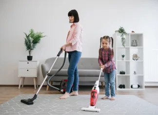 Napake pri nakupu pokončnih sesalnikov, ki jih ne smete storiti! Brunette woman and tween girl utilizing different models of vacuum cleaners while removing dirt in living room. Diligent young homemakers sharing responsibilities of keeping apartment tidy.