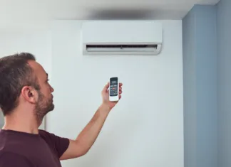 Očistite klimatsko napravo! Iz nje grozi smrtonosna legionela Man holding a modern AC unit remote.