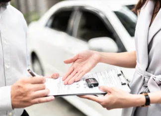 Kaj so »covid avtomobili« in zakaj so trn v peti? Automotive business, car sale or rental concept : Happy customer with car dealer agent making deal and signing on agreement document contract in auto showroom or car dealer office.