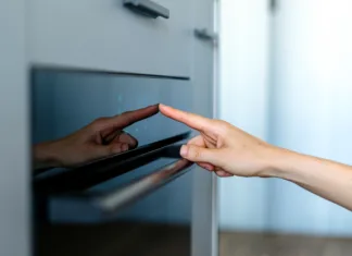 Ali je samočistilna funkcija škodljiva za pečico? Cropped view on woman hand press sensor button of modern electric oven to cooking dinner. Female finger choose program on touch control panel with indicators. Household baking appliances at kitchen