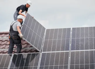 Neurja povzročajo vse več škode na sončnih elektrarnah Men technicians mounting photovoltaic solar moduls on roof of house. Builders in helmets installing solar panel system outdoors. Concept of alternative and renewable energy.
