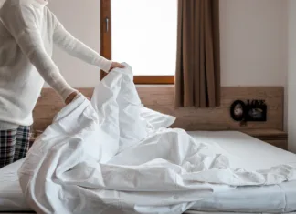 Kako pravilno oprati in sušiti puhasto odejo? Woman making bed in bright bedroom. Maid Cleaning messy hotel bed cushion and duvet, changing bed sheets with clean. Selective focus. Copy space