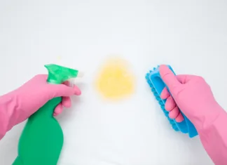 Kako dezinficirati vzmetnico na naraven način? Hands in rubber protective gloves holding spray bottle and brush. White mattress cleaning. Urine stain from baby, kid, children, adult people or pet. Point of view shot. Close up. Top view.