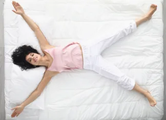 Nasveti za nakup pravega ležišča Top view of happy woman laying like star on white bedding, wake up well rested in morning, king size bed, good relaxation. Chilling on bed in pyjamas at home. Comfort, sleep, rest concept