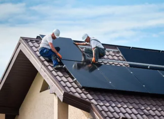 Samooskrba z net meteringom: Spreminja se pogoje za vključitev v sitem Workers building solar panel system on rooftop of house. Two men installers in helmets installing photovoltaic solar module outdoors. Alternative, green and renewable energy generation concept.