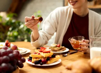 Zakaj so vaflji tako priljubljeni po vsem svetu? Close-up of woman pouring honey on waffles while eating breakfast at dining table.