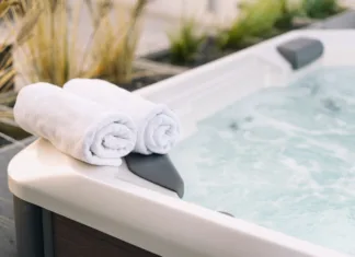 Kako masažni bazen izboljša vaše zdravje? Selective shot of white dry towel folded on edge of hot tub in natural sunlight on residential backyard garden. Bath on terrace. Bathtub with bubble water on hotel roof at sunset light