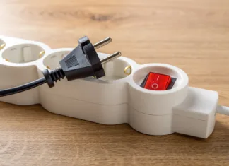 Teh treh električnih naprav nikoli ne izklapljajte iz električnega omrežja: obstaja zelo dober razlog! Unplugged electric appliance plug over switched off white power strip on the floor. Power crisis. Increasing the energy costs, heating costs, save electricity concepts. Power outage. Close-up.