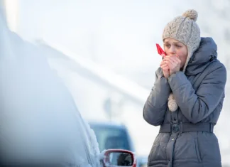 Ogrevanje avtomobila pozimi, preden sedete vanj, je zelo škodljivo! Young woman cleaning her car from snow and frost on a winter morning, she is freezing and needs to get to work