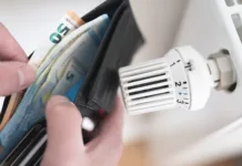 5 zimskih napak v domu, ki praznijo denarnico close-up view of person holding wallet with cash next to turned down thermostat on radiator, rising energy and heating costs concept