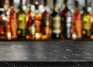 Kakšen je rok trajanja alkoholnih pijač po odprtju? Nekatere bi vas lahko neprijetno presenetile … Grey table top and beautiful bokeh shelves with alcohol bottles at the background. Bar concept.