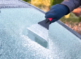 Nič več ne boste zmrzovali ob strganju stekel: triki, ki vam pozimi olajšajo delo … Hand wearing blue glove scratching ice from car window. The ice scraper is an extension of the arm. Part of the windshield is ice free. Only part of the window is visible. Symbol or concept of winter season, cold, frost, weather, sight.