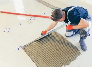 Ali se začne s talnimi ali stenskimi ploščicami? A male construction worker installs a large ceramic tile