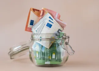 Kako upravljati finance in prihraniti do 500 € na leto Euro cash banknote in glass jar on beige background. Saving money concept crisis and inflation Consumption and economy Collecting money. Tips. Extra money, passive