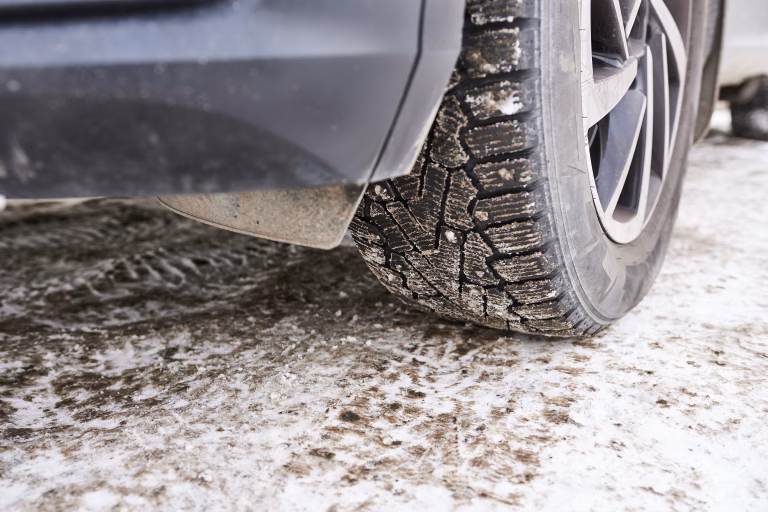 Close-up of a car wheel with mud on the road. A studded winter tyre.