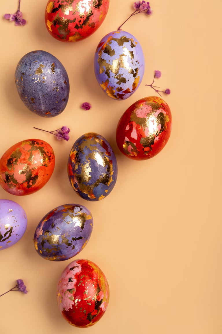 Happy Easter day! Сomposition with modern Easter eggs with gold decorations and spring flowers on beige background. Easter holiday background with stylish eggs decorations. Flat lay, copy space.