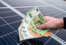 64 milijonov vreden razpis za sofinanciranje sončnih in vetrnih elektrarn beautiful young hands in black hold a sum of euros in front of solar panels. Green electricity concept