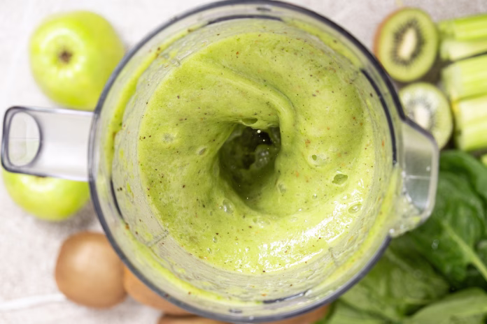 Making a green smoothie with celery, kiwi, apple and spinach in a blender, top view
