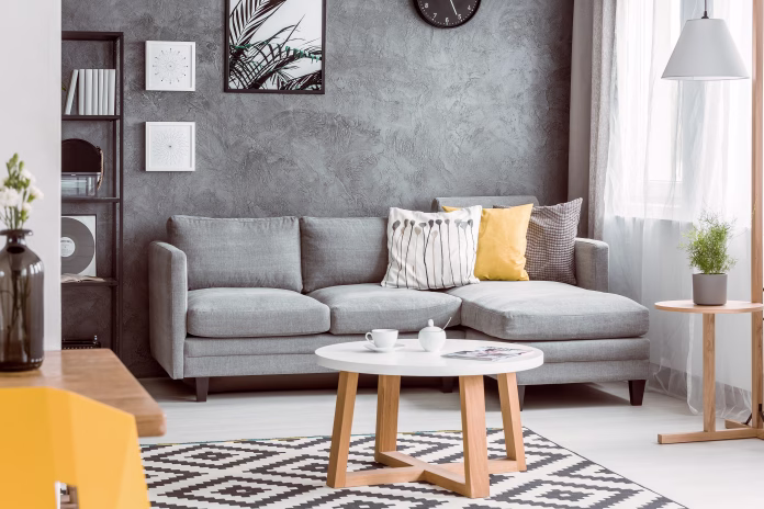 Wooden coffee table on black and white carpet in living room with yellow pillow on grey sofa