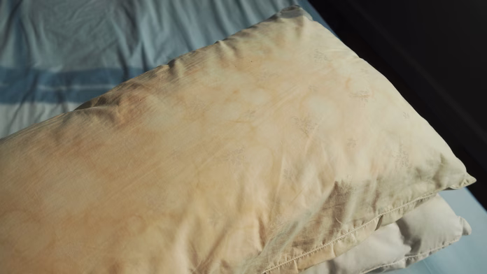Dirty pillow from saliva stain on the bed. Dirty pillow with pale yellow and brown color.