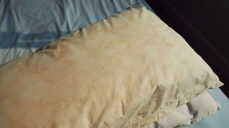 Dirty pillow from saliva stain on the bed. Dirty pillow with pale yellow and brown color.