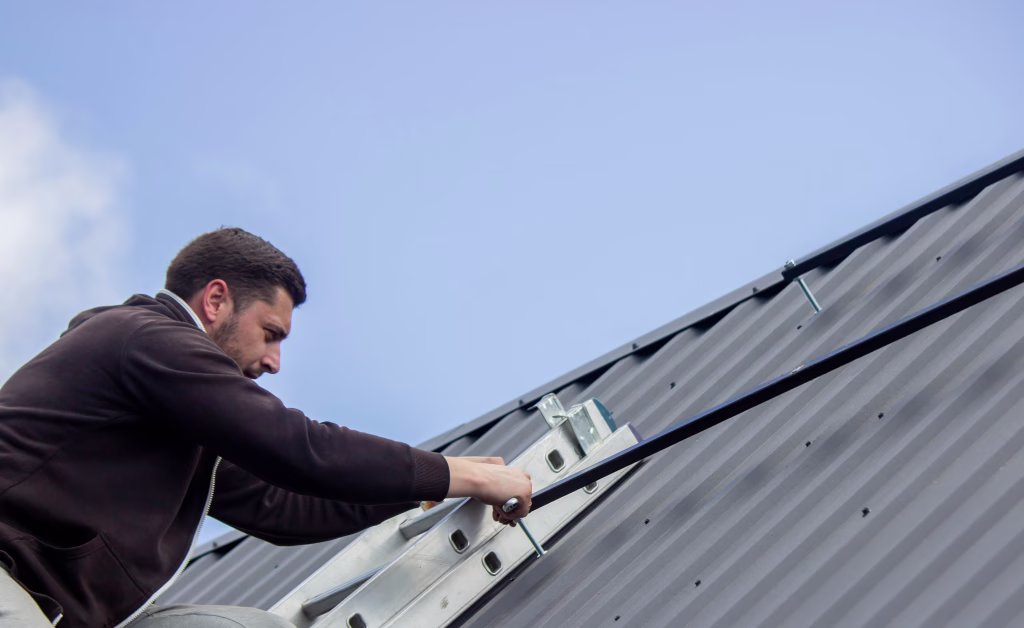 A man is installing solar panel mounts on the roof. Selective focus.