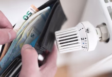 Toplejši dom in nižji računi: kaj storiti z radiatorji pred koncem leta? close-up view of person holding wallet with cash next to turned down thermostat on radiator, rising energy and heating costs concept