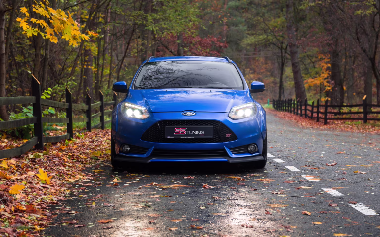 Front view of sporty Ford Focus hatchback on a rural road on rainy autumn day with lots of fallen leaves. Ukraine - October 31 2017