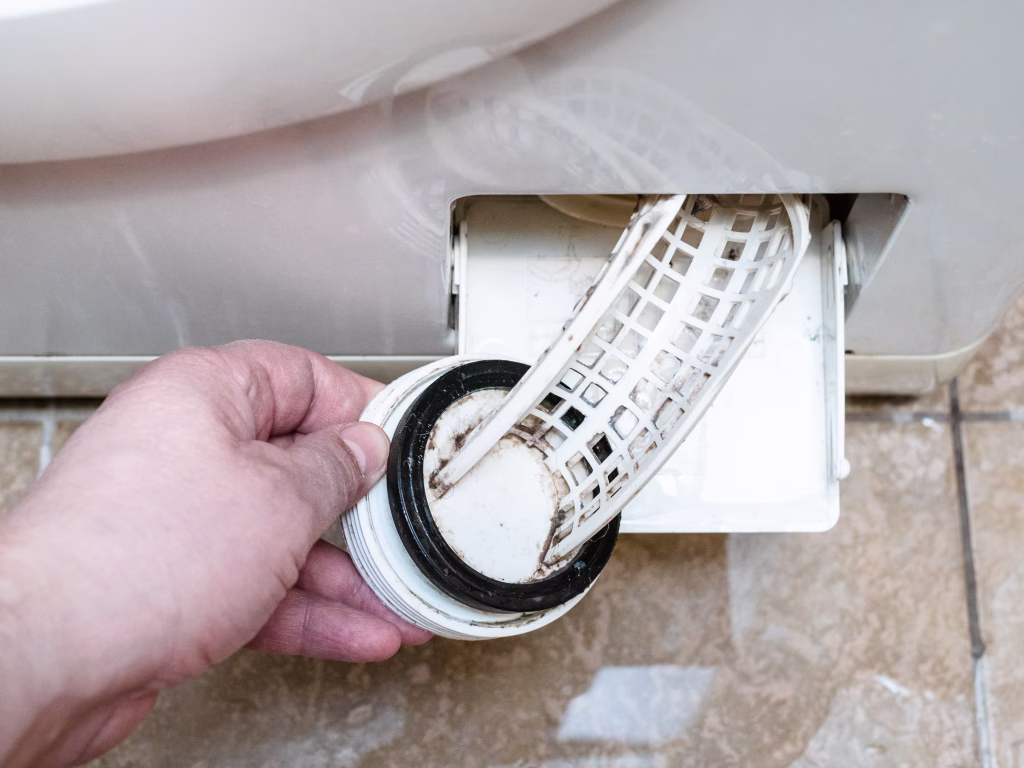 opening of the filter of old washing machine and water puddle on ceramic floor