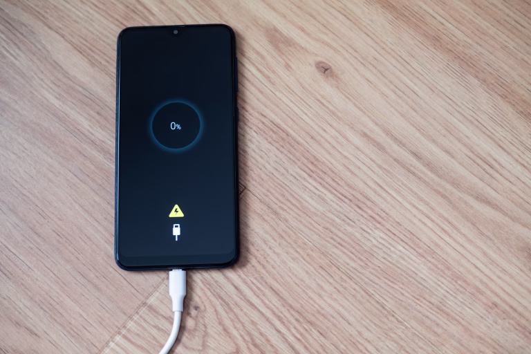 White charging cable plugged into smartphone displaying 0% battery on wooden table, emphasizing urgent need for power in modern life. Essential connection for daily communication