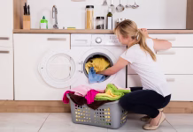 Resnica o tem, zakaj imajo nekateri pralni stroj kar v kuhinji Young Woman Loading Clothes Into Washing Machine In Kitchen