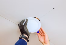 5 naprav, ki zmanjšajo račun za elektriko: že prvi mesec vas bo poraba presenetila An electrician is carefully placing recessed light fixture into ceiling opening, during home renovation skills.