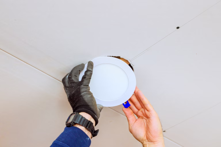 An electrician is carefully placing recessed light fixture into ceiling opening, during home renovation skills.