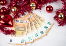 Takšno božičnico bodo zaposleni prejeli že letos Christmas money business concept: some fifty euro banknotes with red and gold baubles and wreath decoration on light wooden table