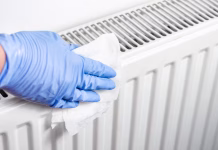 Trik za tople radiatorje: prihranili boste čas in denar med ogrevalno sezono Man with surgical gloves cleaning the radiator with disinfectant wet wipes . Preventing of bacteria and coronavirus spreading .