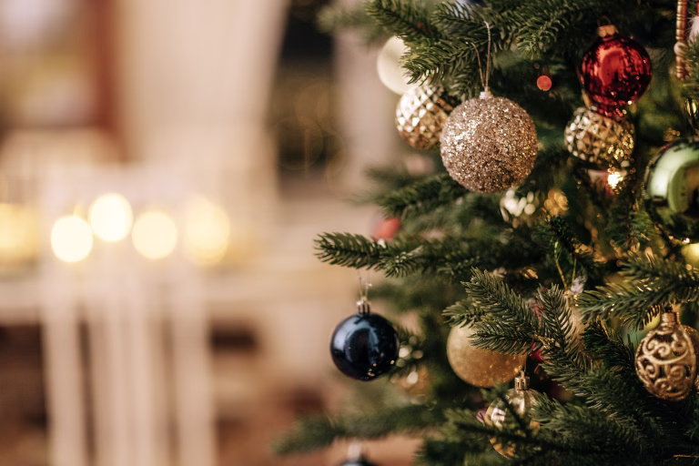 A close-up of a decorated Christmas tree with vintage glass toys. Stylish rich interior with fireplace and lighted candles. New year decorations. Copy space.