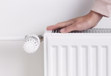 Pustiti ogrevanje vklopljeno vso noč ali ne: Premislite o tem iz tega ključnega razloga … A woman warming her hands on a heating radiator, the concept of conserving heat and energy and the importance of resource management during colder seasons. seeking warmth, energy efficiency, and mindful living