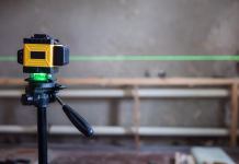 Kaj je vagris? A laser level mounted on a tripod projects a green line onto a construction site. A laser level is essential for precise alignment and measurements in construction projects..