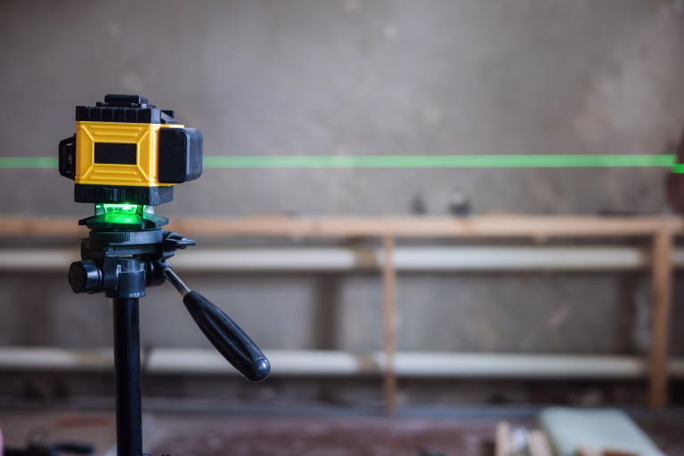 A laser level mounted on a tripod projects a green line onto a construction site. A laser level is essential for precise alignment and measurements in construction projects..
