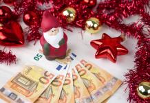 Božičnice in zimski regres: eni dobijo 639 evrov, drugi več kot 14.000 Christmas money business concept: a statuette of Santa Claus on some fifty euro banknotes with red and gold baubles and wreath decoration on light wooden table