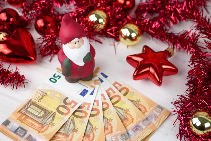 Christmas money business concept: a statuette of Santa Claus on some fifty euro banknotes with red and gold baubles and wreath decoration on light wooden table