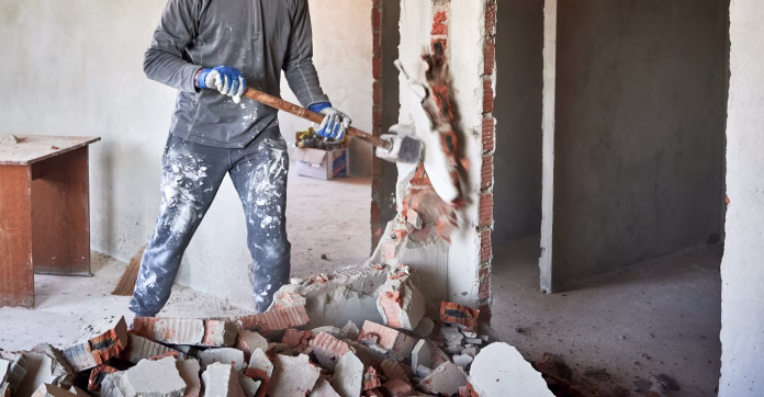 close-up-of-sledgehammer-blow-on-brick-plaster-workman-striking-devastating-blow-at-remnants-of-interoom-wall-against-backdrop-of-table-and-other-plastered-walls-stockpack-istock Close up of sledgehammer blow on brick, plaster. Workman striking devastating blow at remnants of interoom wall against backdrop of table and other plastered walls.