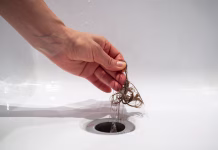 Strokovnjaki svetujejo! Kis ni rešitev za zamašene odtoke, tukaj je tisto, kar res deluje Hand pulls hair out of bathroom drain. Female palm extracts shock of hair from siphon in bathroom. Water drain hole clogged with hair clump. Close up. Cleaning shower polluted sewerage system.