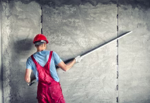 Najpogostejše napake pri strojnih ometih: kako pomembna je priprava industrial worker with plastering tools renovating a house. builder worker plastering facade industrial building with leveler