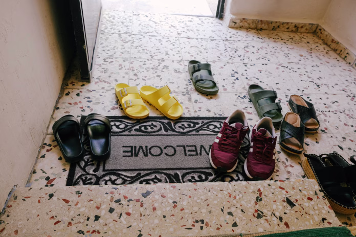 Welcome Doormat Surrounded by Various Shoes at a Home Entrance