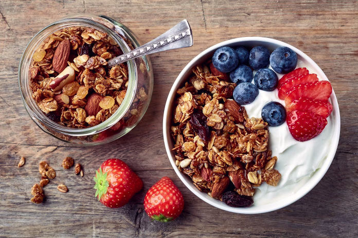 Bowl of homemade granola with yogurt and fresh berries on wooden background from top view