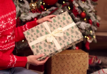 5 stvari, ki jih nikoli (res nikoli) ne podarjajte med prazniki: v hišo privabljajo nesrečo in bedo Close-up of New Year's gift with a bow in hands. Gift in a box with festive packaging and a bow. Christmas or New Year. To take or to put a gift. Surprise. Girl examines a box in a gift wrapping